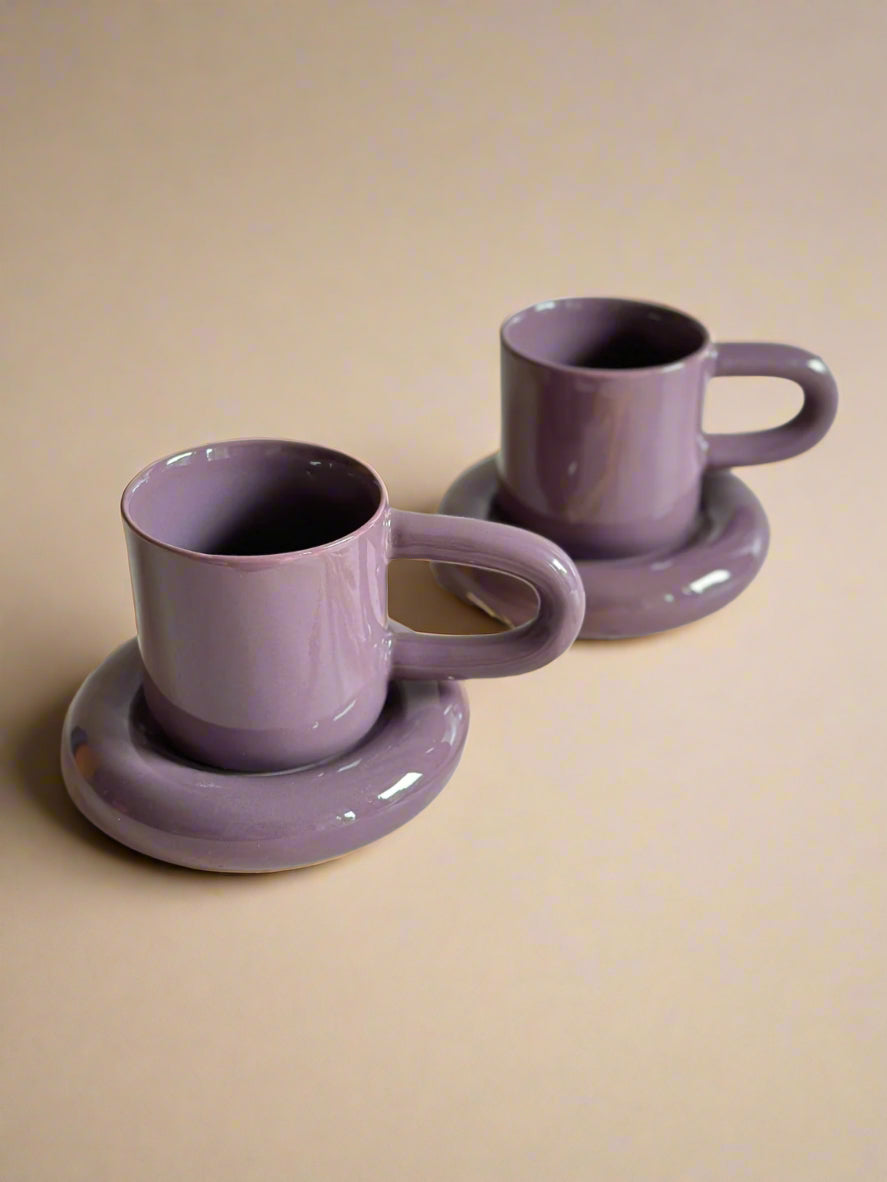 two purple cups and saucers sitting on a table