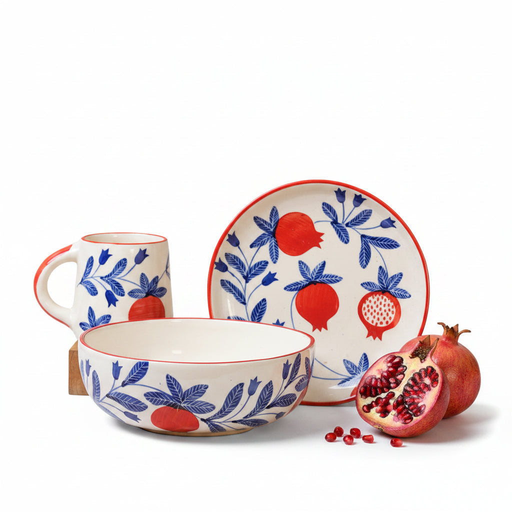 Ceramic set with bowl, mug, and plate featuring red pomegranate and blue leaf design on a beige background