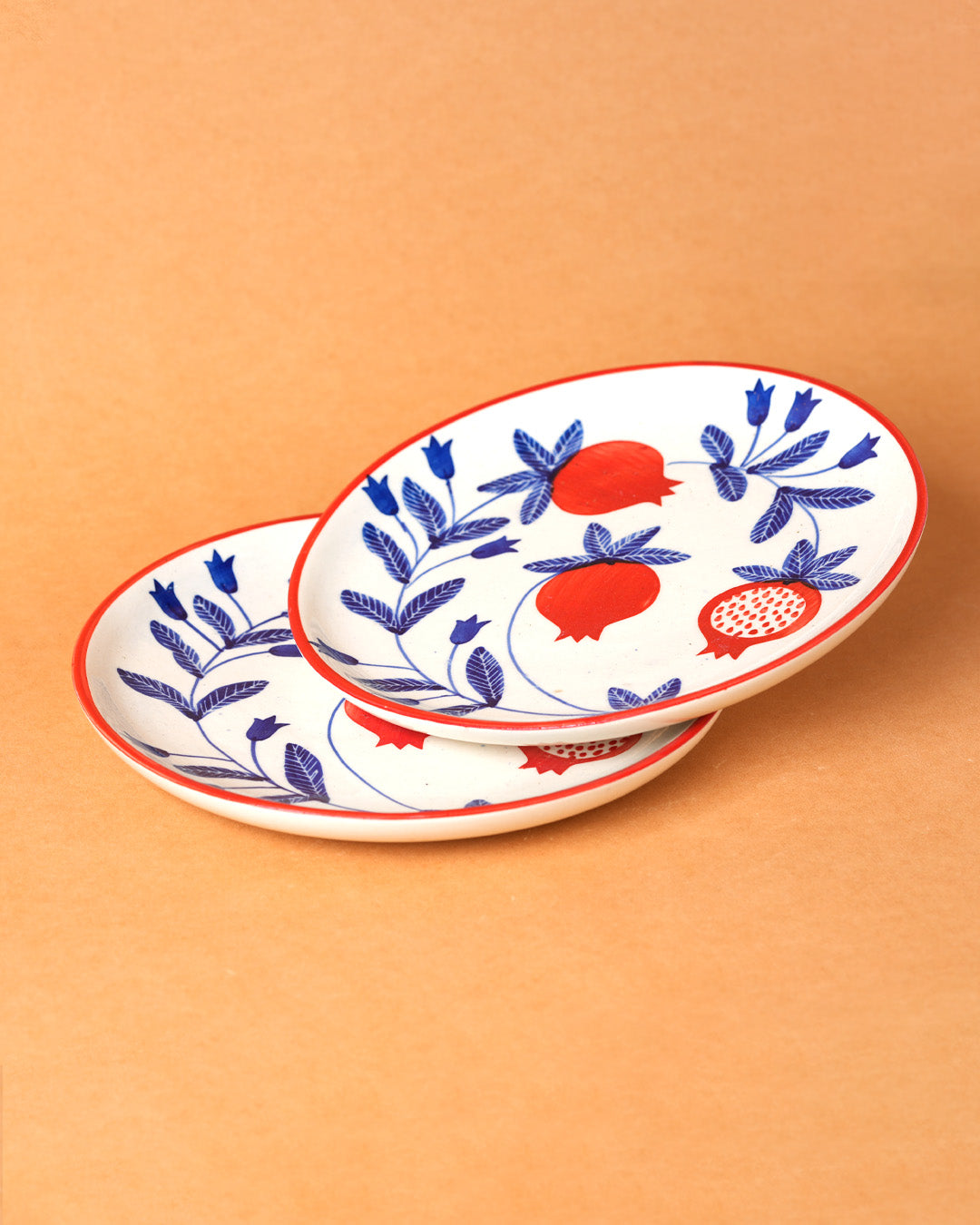 Two decorative plates with blue floral patterns and red pomegranate designs on a beige background