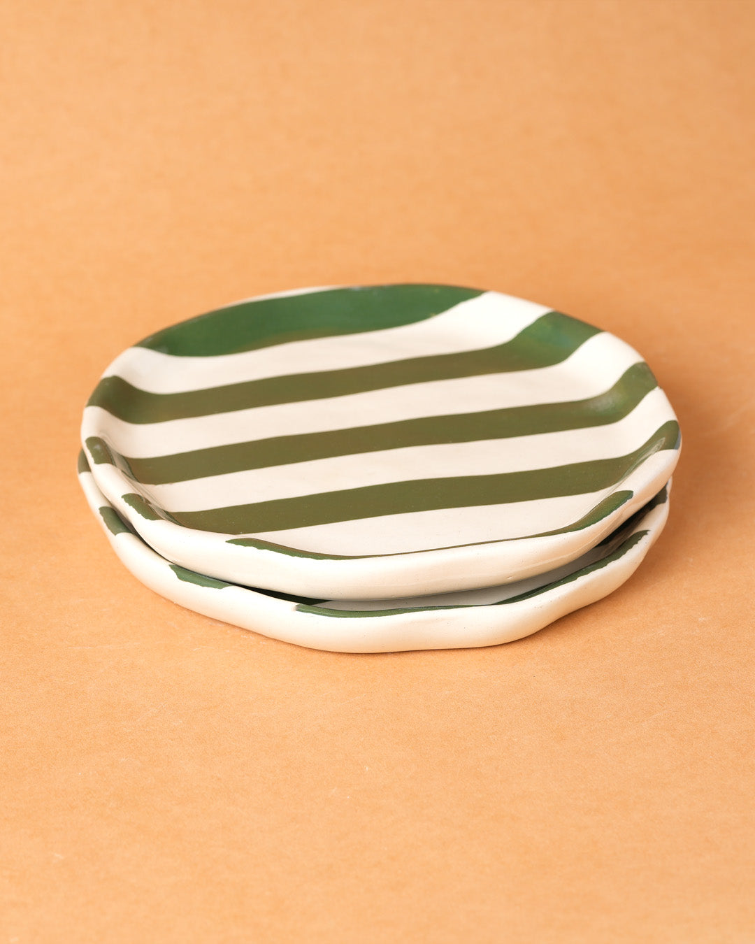 Two green and white striped ceramic plates on a beige background
