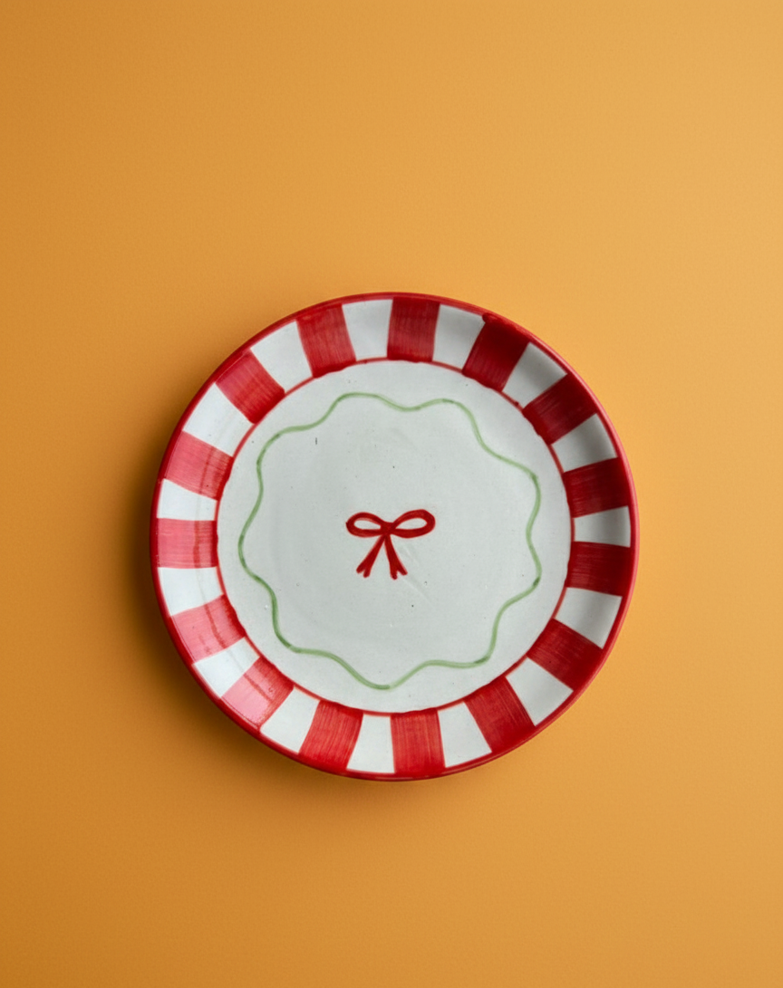 Decorative plate with red and white stripes and a red bow on an orange background