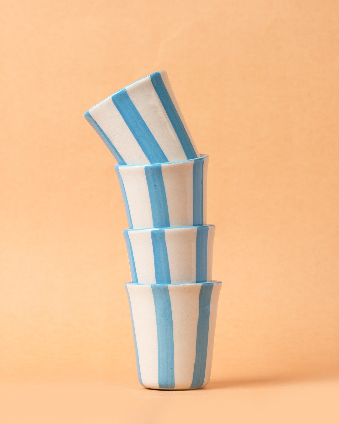 Stack of four ceramic bowls with blue and white stripes on a peach background