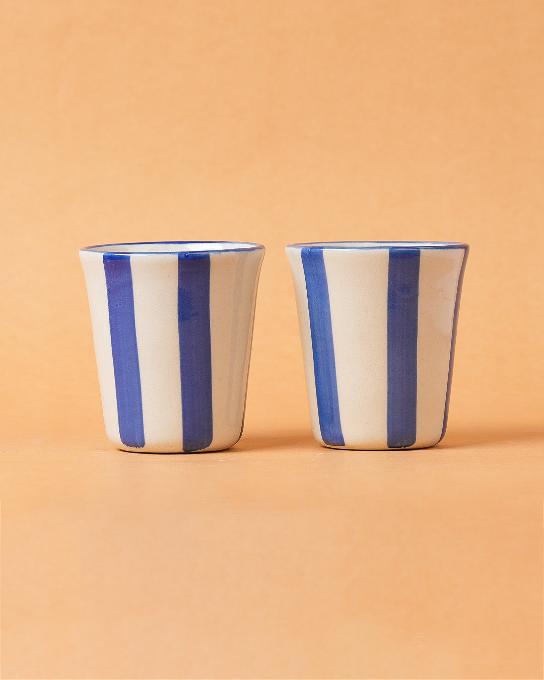 Two ceramic cups with blue stripes on a beige background