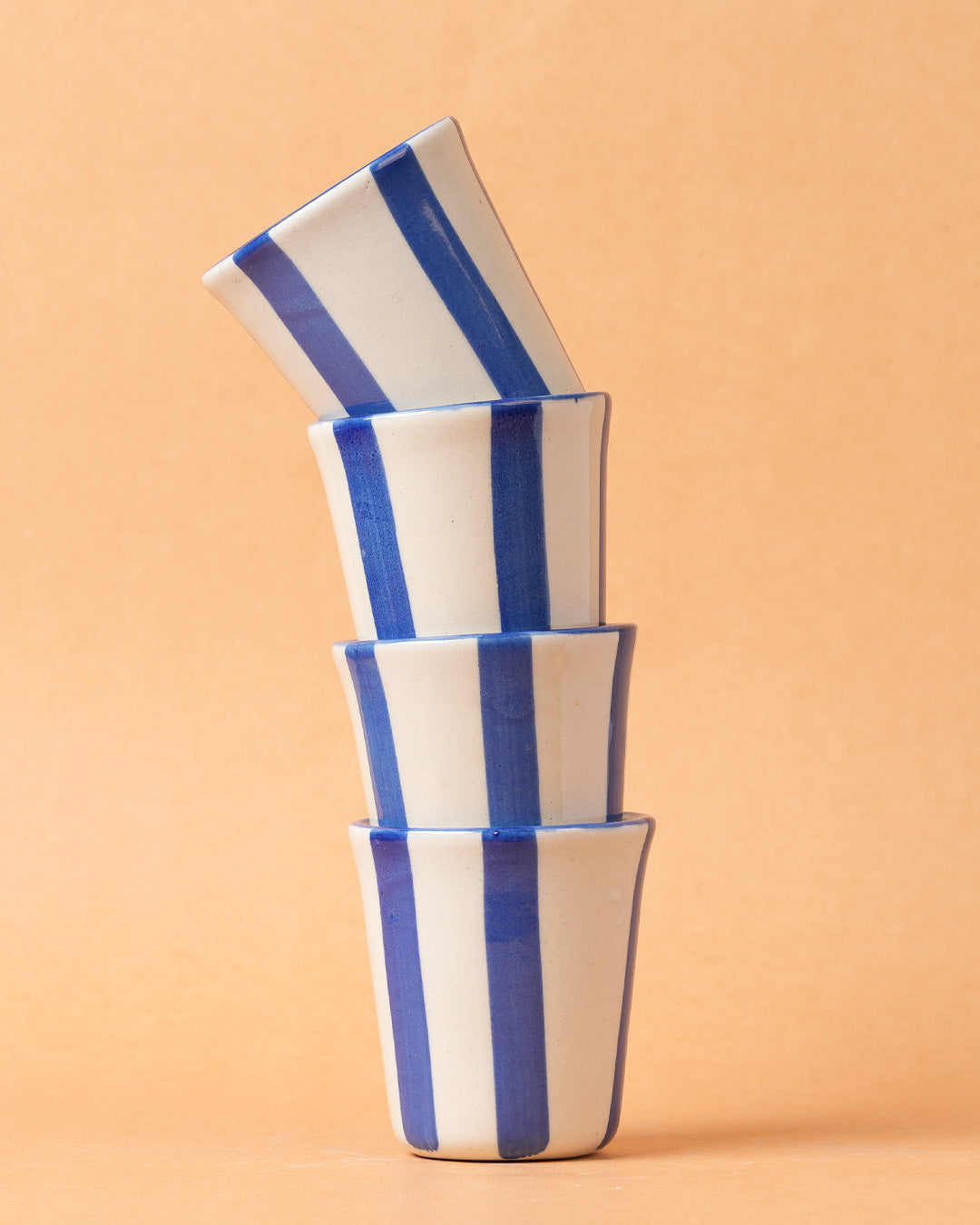 Stack of four blue and white striped ceramic cups on a beige background