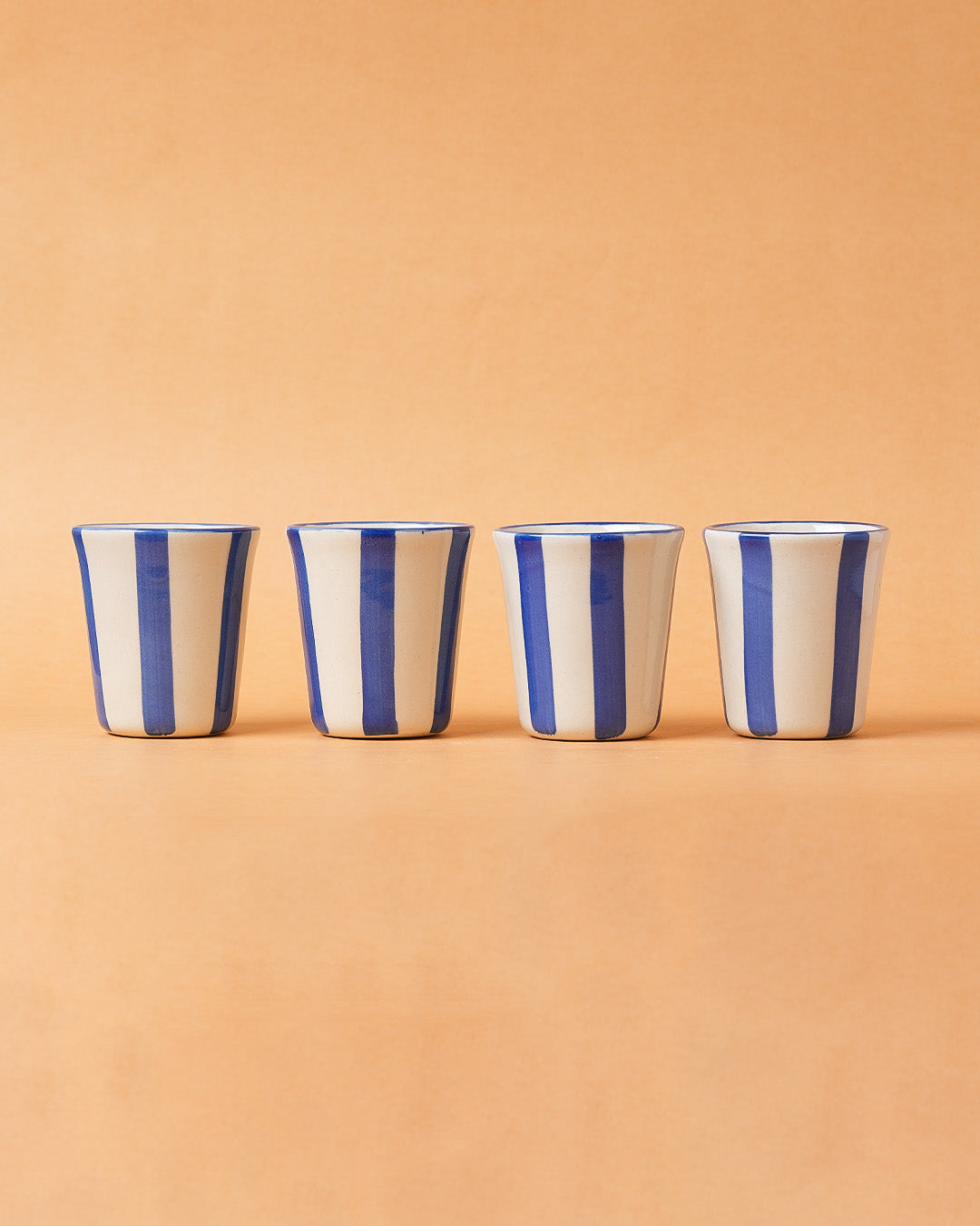 Four ceramic cups with blue and white stripes on a beige background