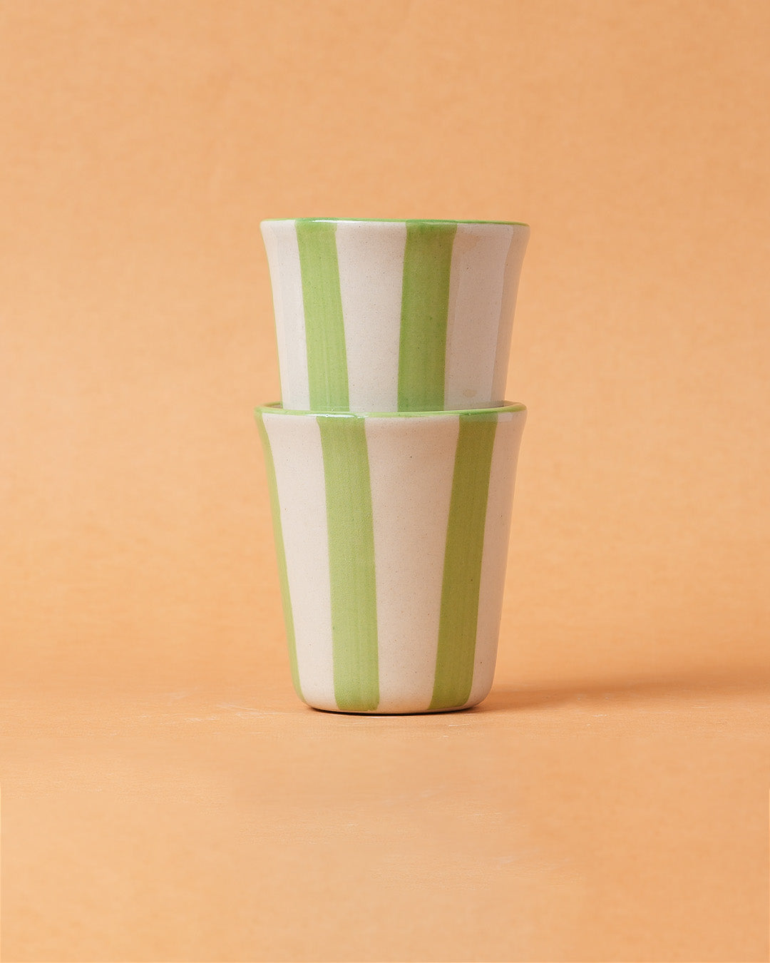 Two stacked ceramic cups with green and white stripes on a peach background