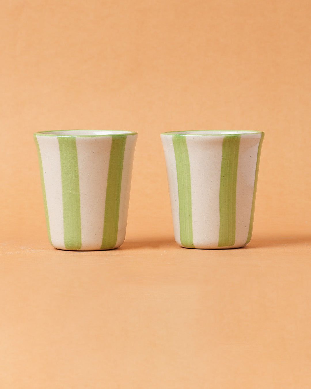 Two ceramic cups with green stripes on a peach background