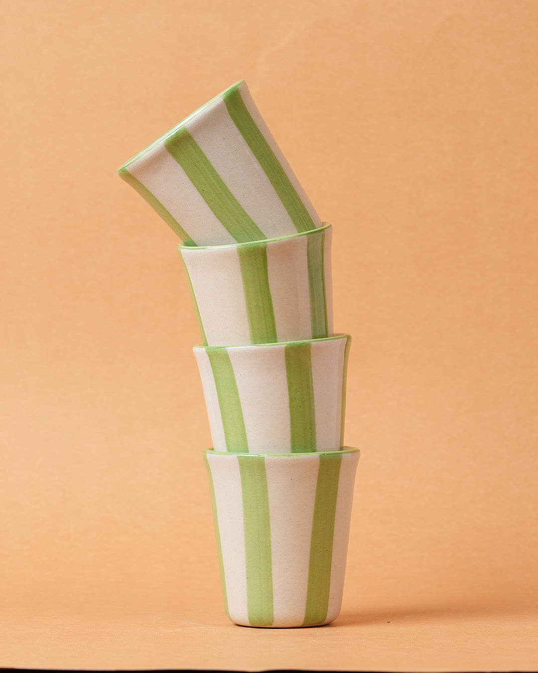 Stack of four ceramic pots with green stripes on a peach background