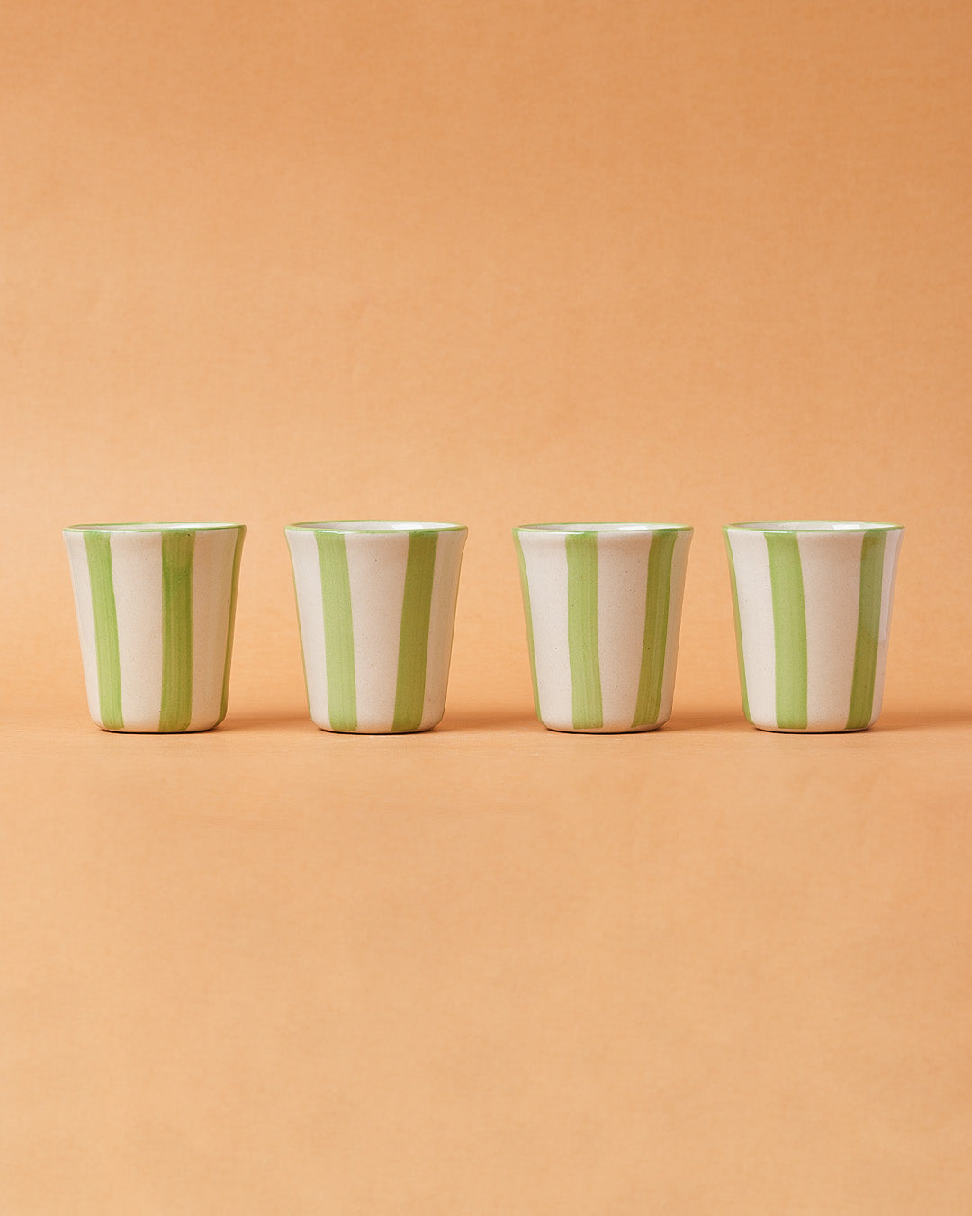 Four ceramic cups with green and white stripes on a peach background