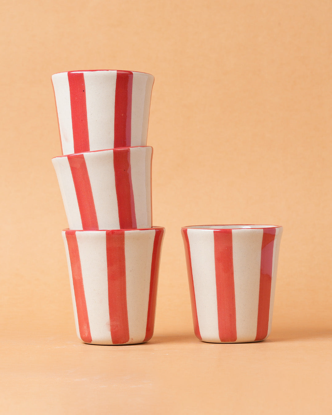 Stack of red and white striped ceramic cups on a beige background