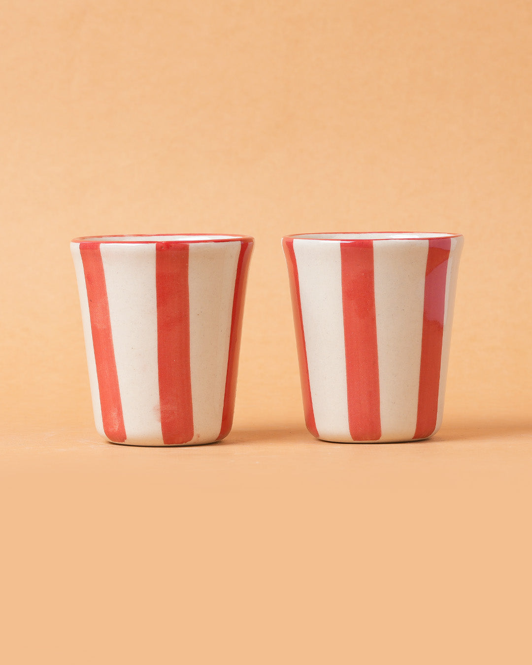 Two red and white striped ceramic cups on a beige background
