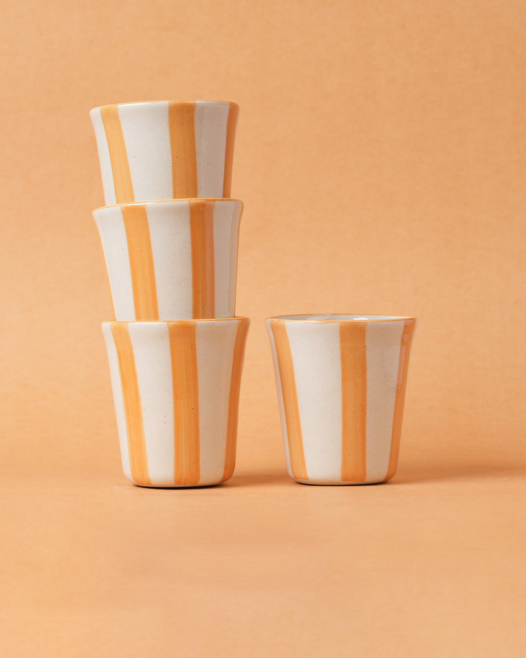 Stack of four ceramic cups with orange and white stripes on a peach background