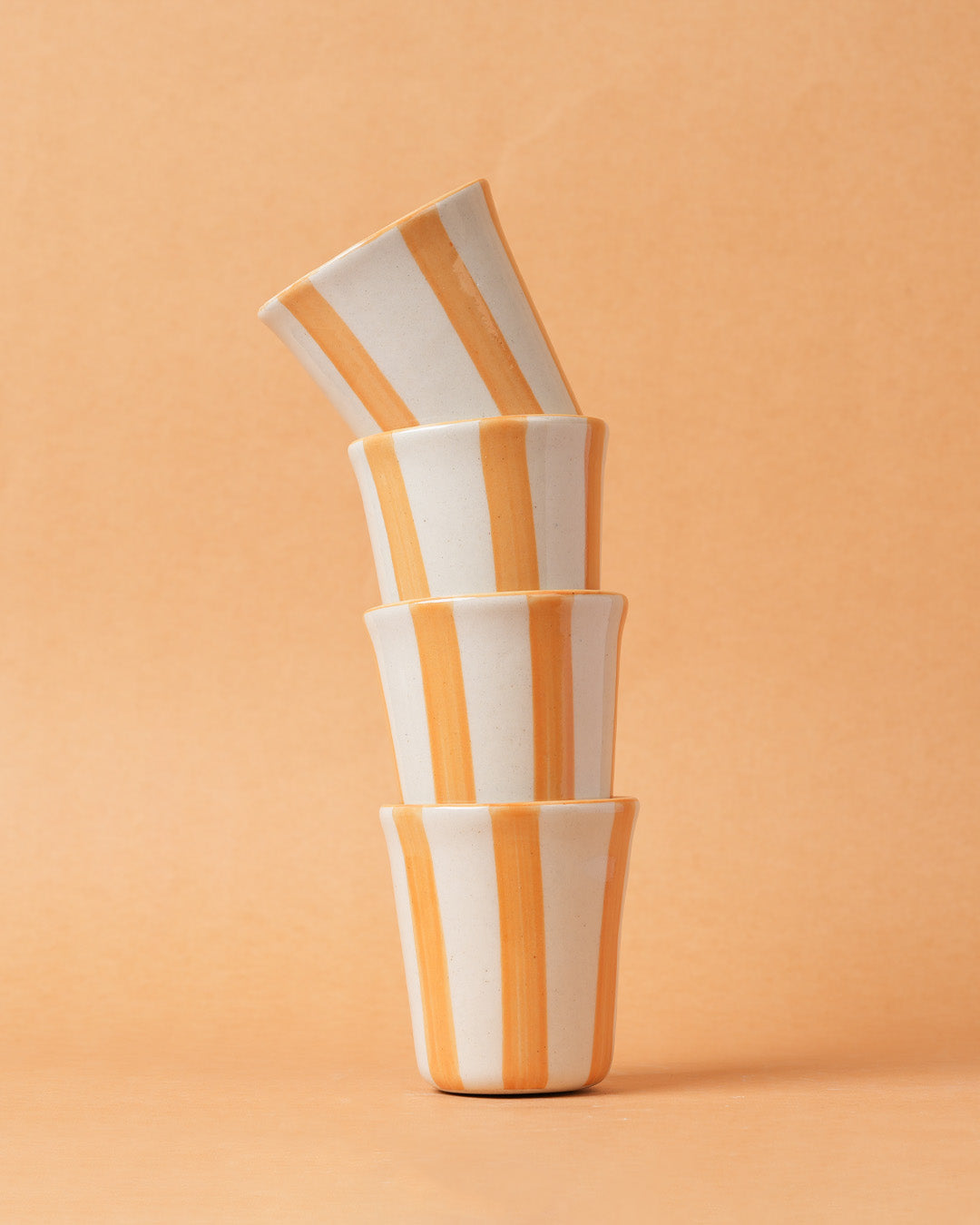Stack of four striped ceramic cups on a peach background
