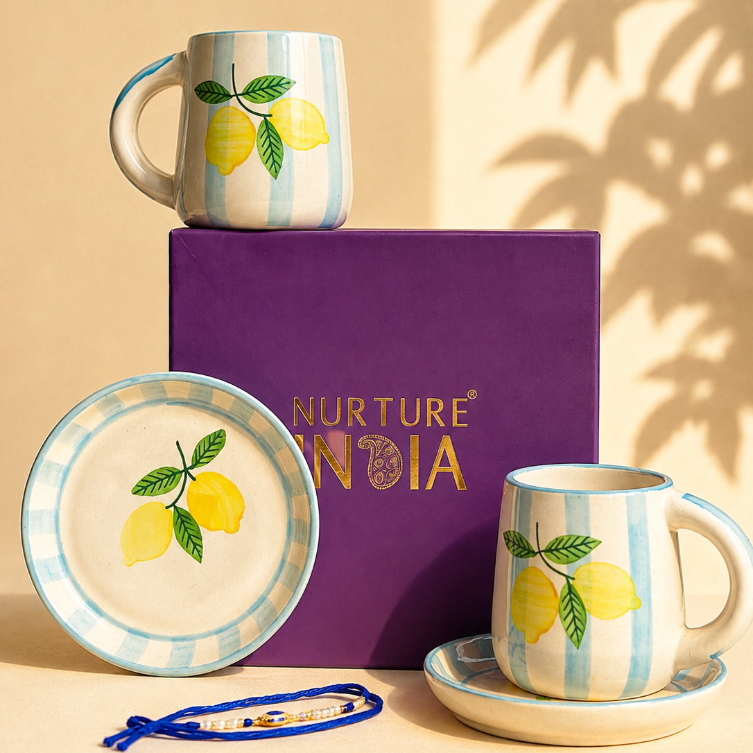 A ceramic mug, matching saucer, and plate set with a lemon illustration and light blue-and-white stripes, displayed with a purple Nurture India gift box and a small blue bracelet on a warm beige background.