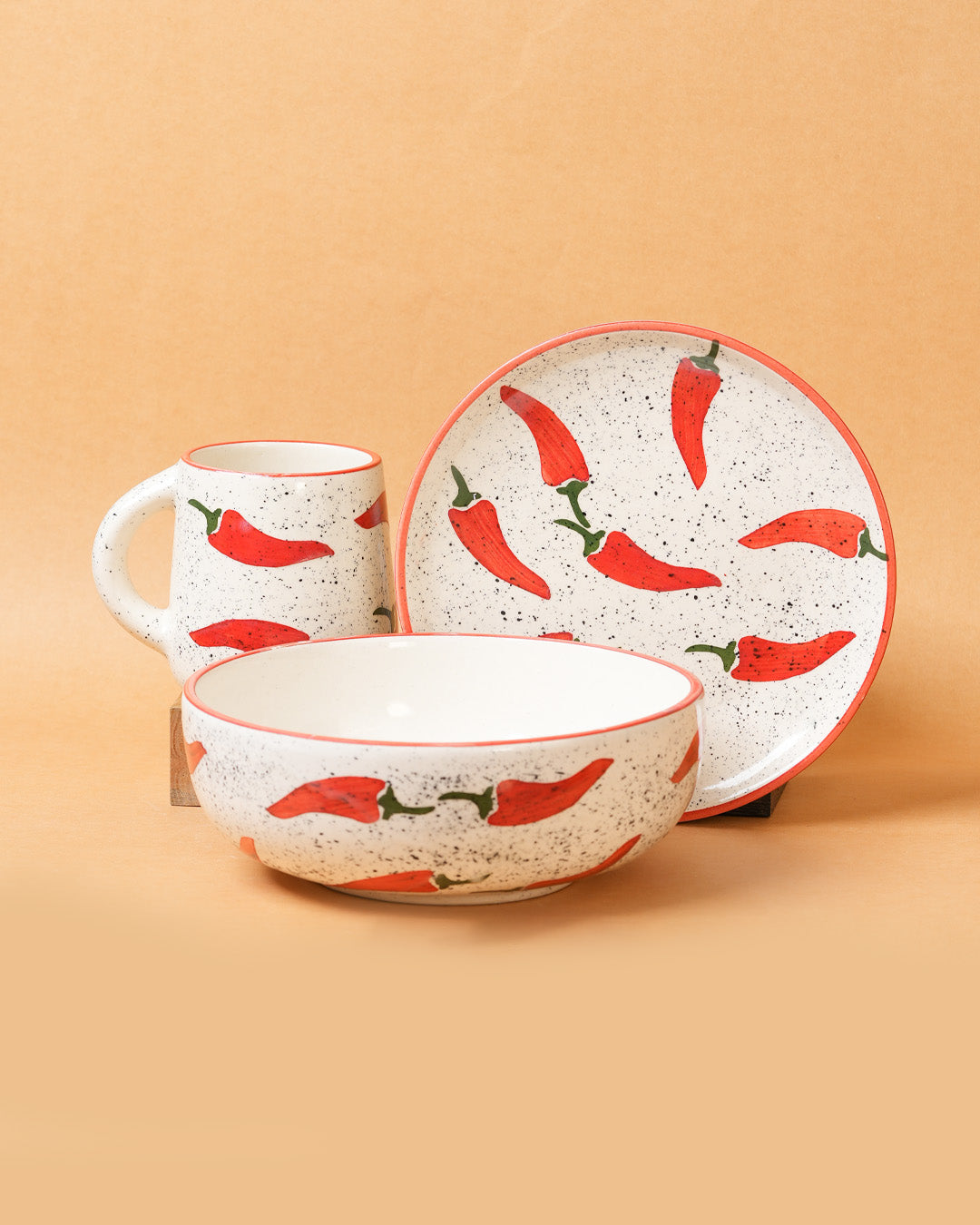 Ceramic set with bowl, mug, and plate featuring red chili pepper design on a beige background