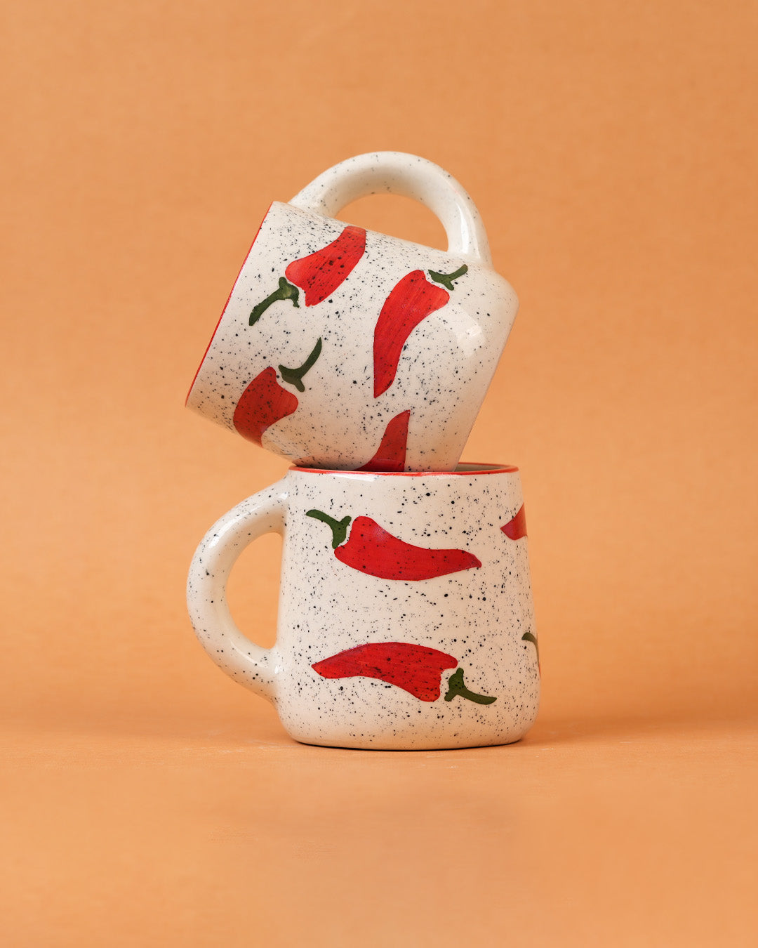 Two ceramic mugs with red chili pepper design on a beige background