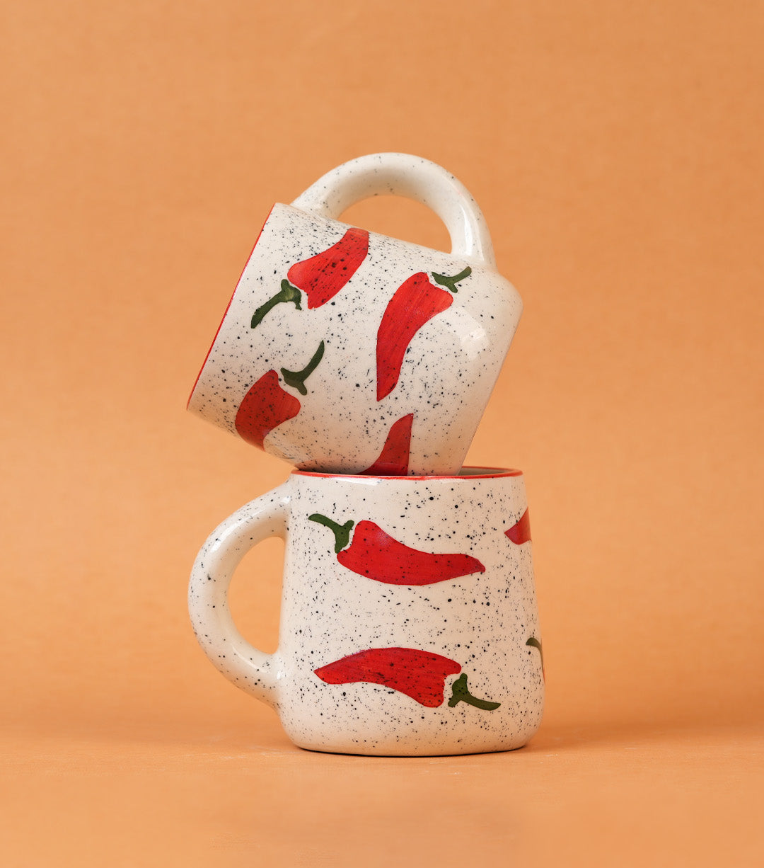 Two ceramic mugs with red chili pepper design on a beige background