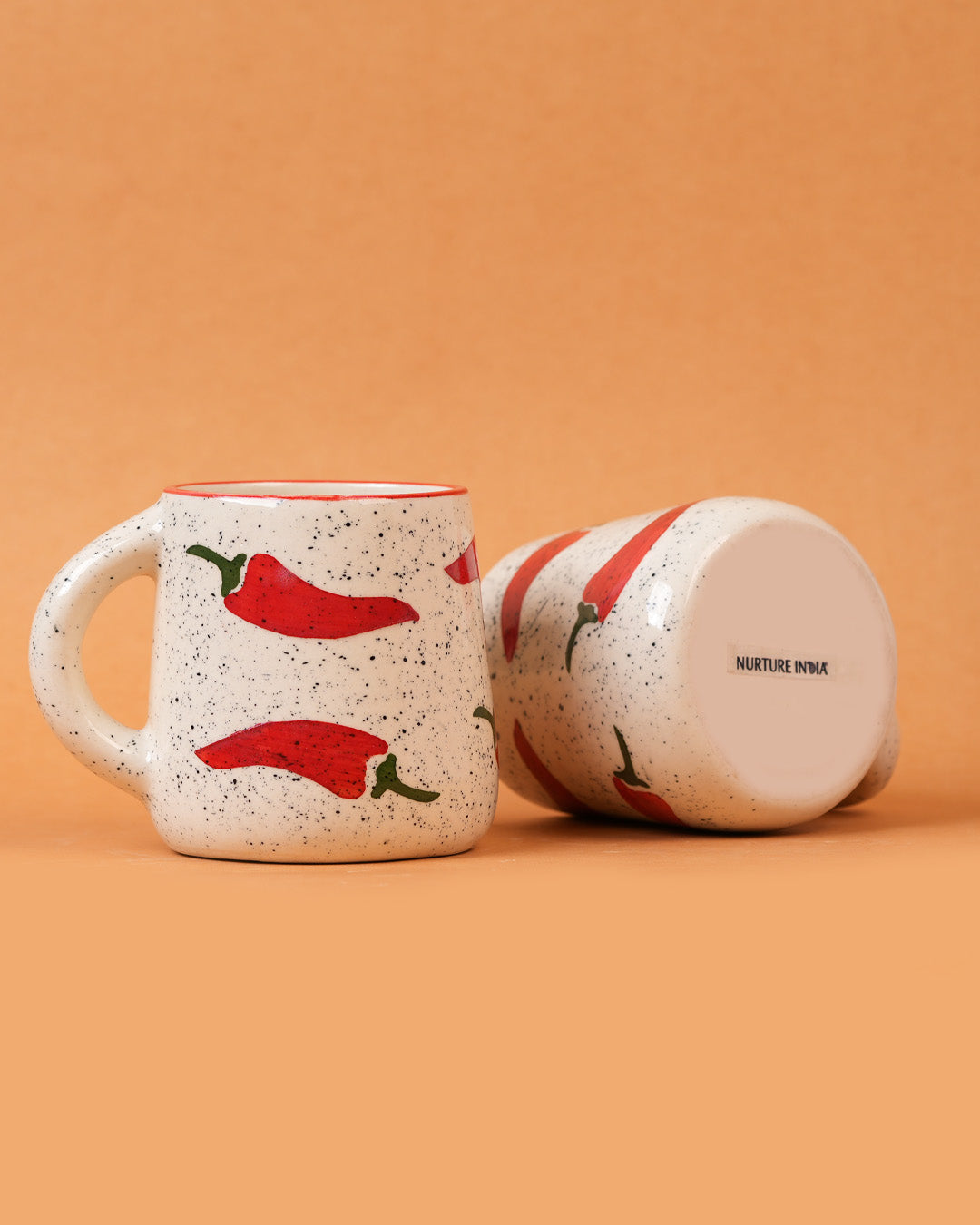 Speckled ceramic mug with red chili pepper design on an orange background