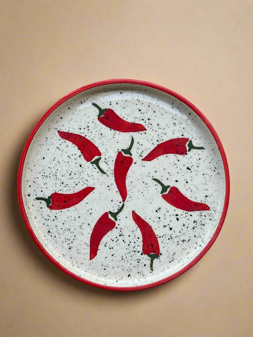 Speckled ceramic plate with red chili pepper design on a gray surface