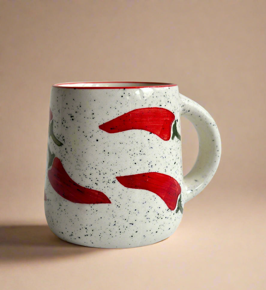 Speckled ceramic mug with red chili pepper design on a beige background