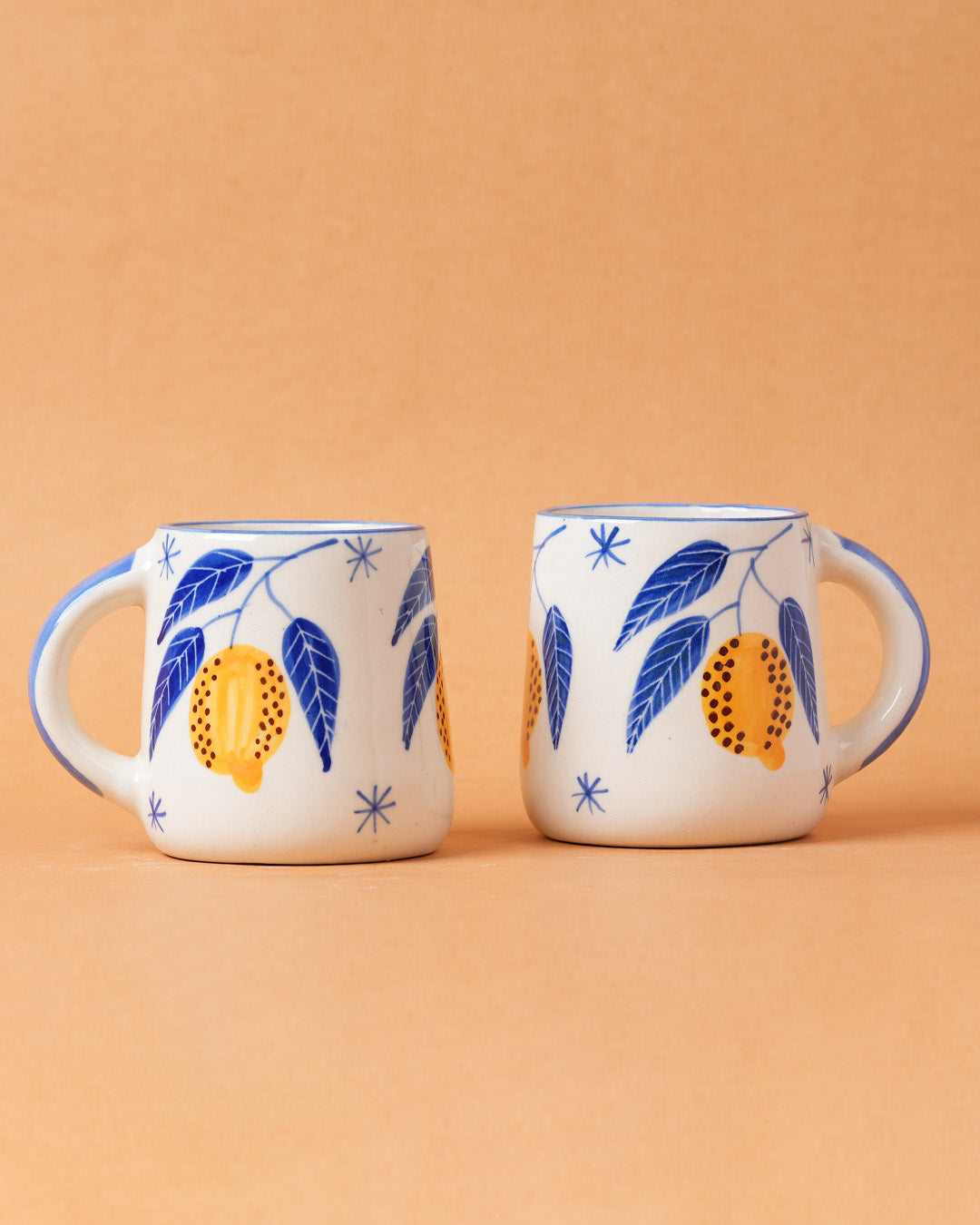 Two ceramic mugs with leaf and fruit design on a beige background