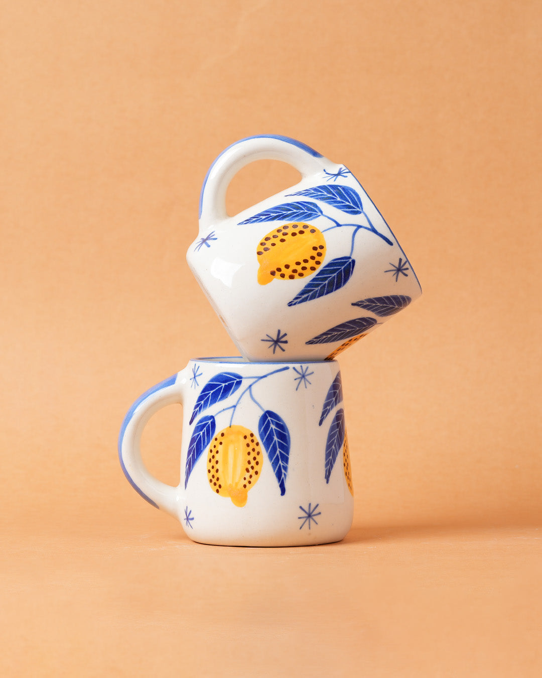 Two ceramic mugs with floral designs stacked on a beige background