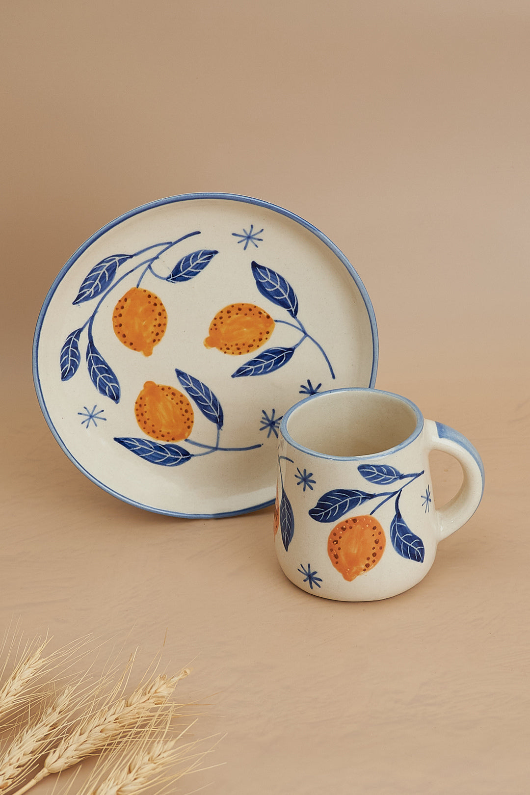 Ceramic mug and plate set with orange and leaf design on a beige background