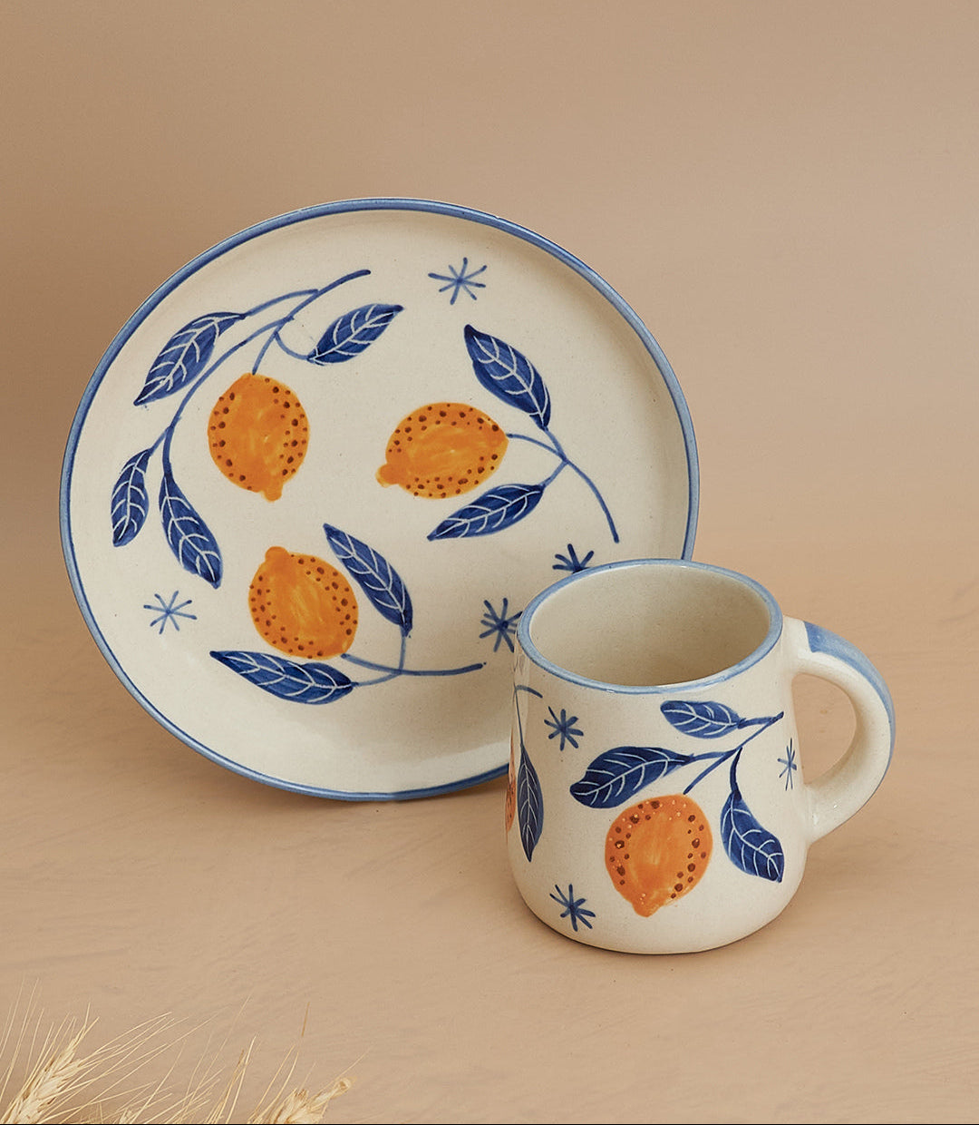 Ceramic mug and plate set with orange and leaf design on a beige background