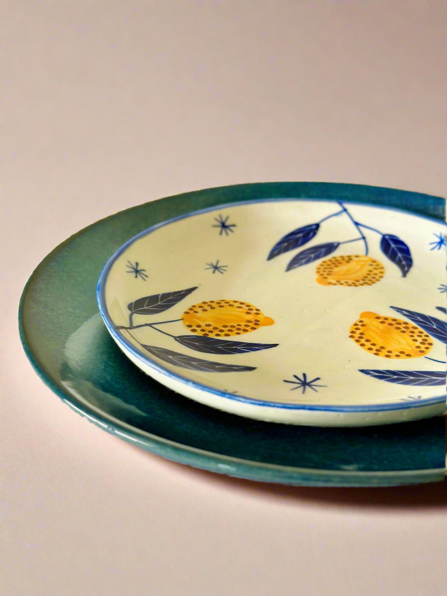 Two ceramic plates stacked on a beige background, one with a green rim and the other with a decorative yellow and blue design.