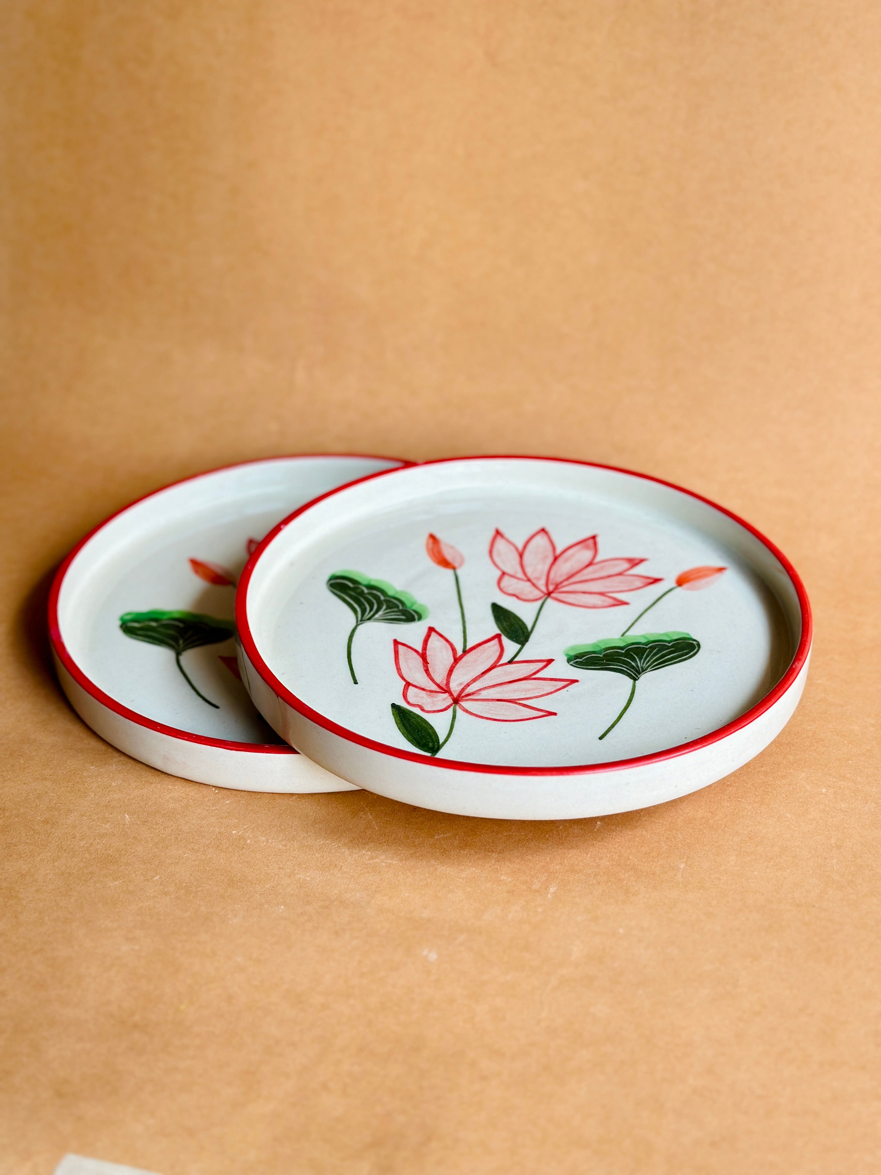 Two ceramic coasters with lotus flower design on a brown background