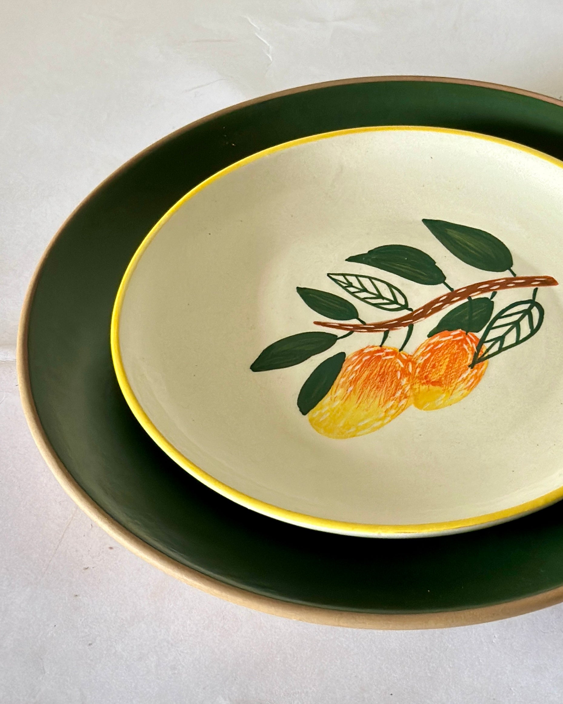 Two ceramic plates stacked on a light gray background, with one plate featuring a design of oranges and leaves.