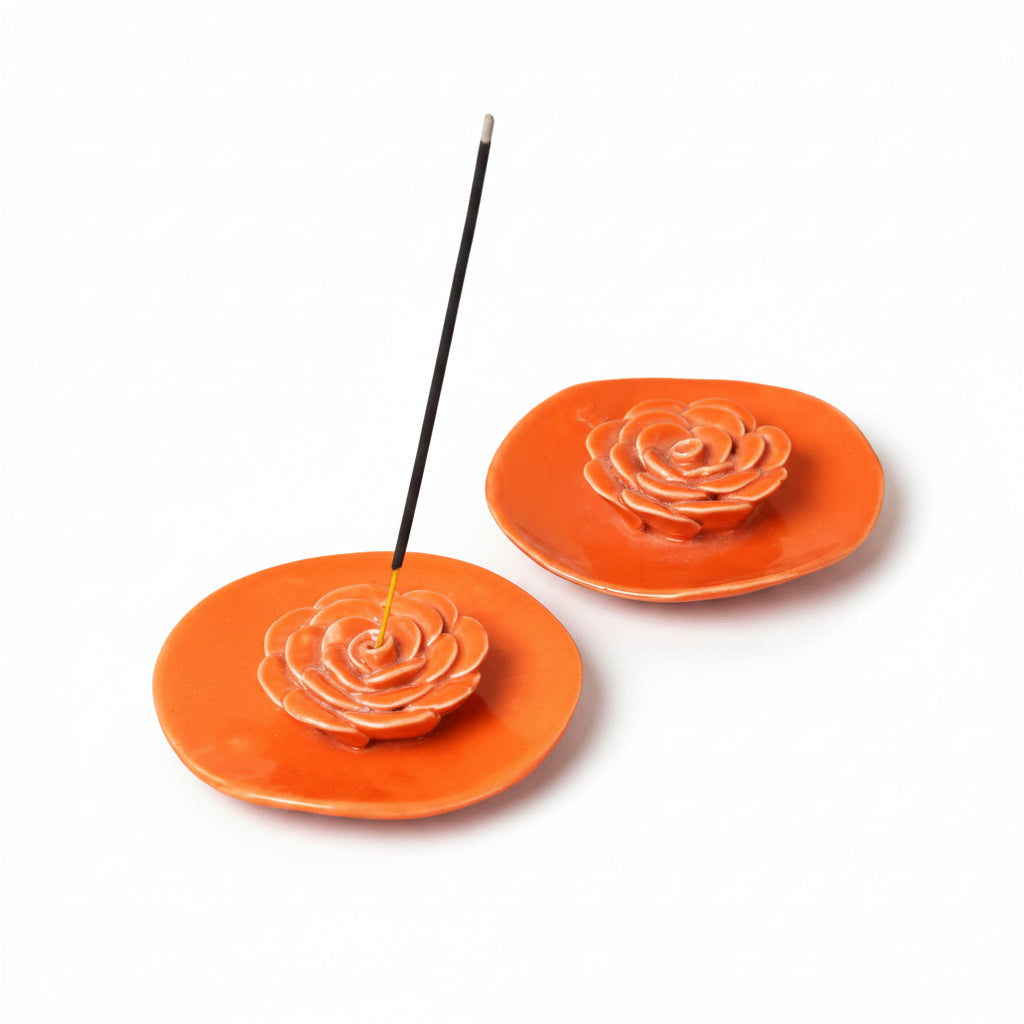 Two orange ceramic incense holders with rose designs on a beige background