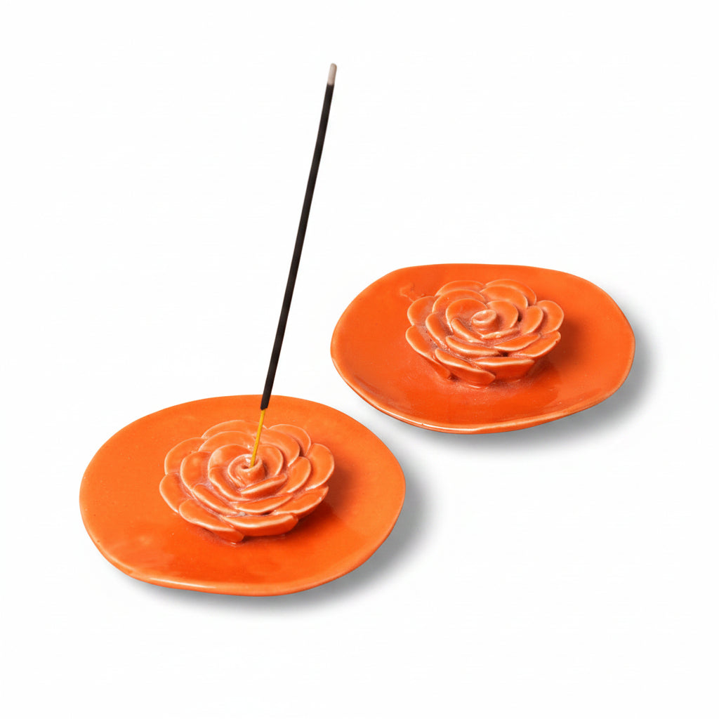 Two orange ceramic incense holders with rose designs on a beige background