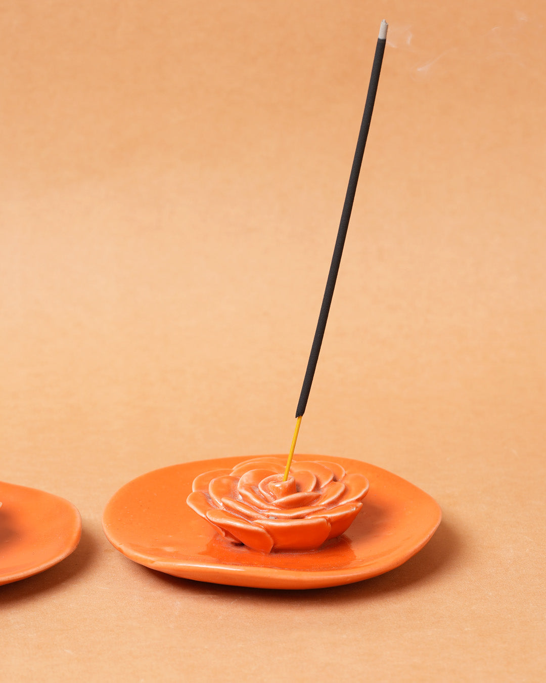 Incense stick on an orange rose-shaped incense holder against a beige background