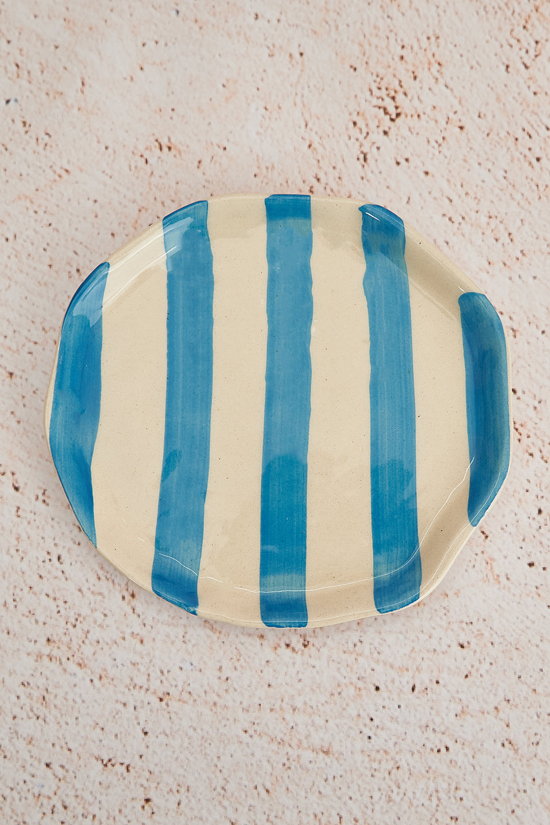 Ceramic plate with blue and white stripes on a textured beige surface