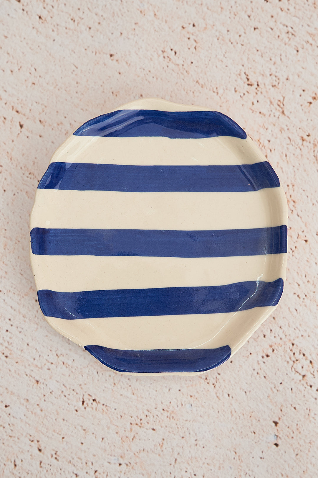 Round ceramic plate with blue and white stripes on a textured beige surface