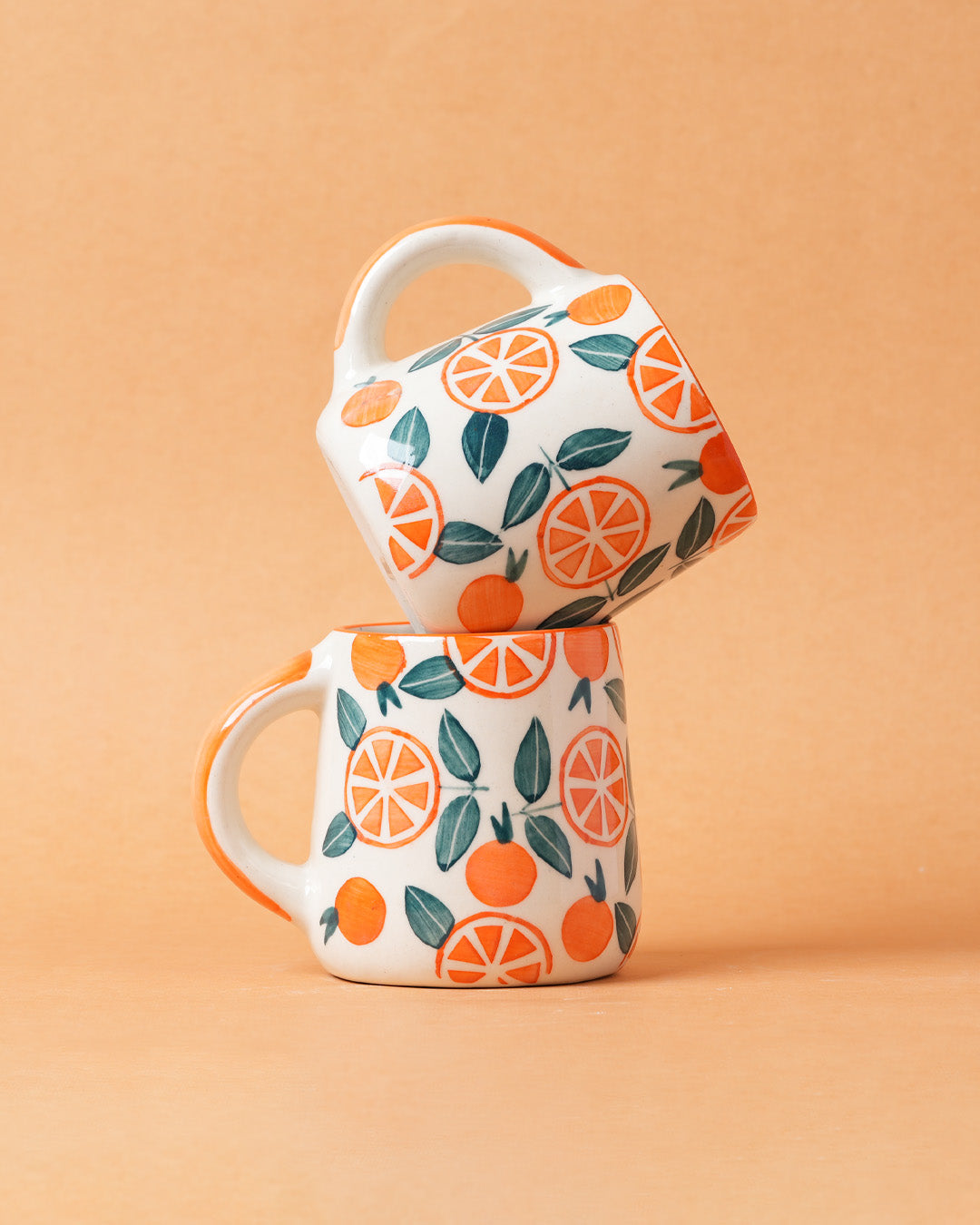 Two mugs with orange and leaf pattern stacked on a beige background
