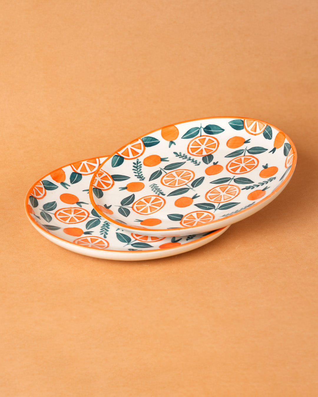 Two ceramic plates with orange and leaf pattern on a beige background