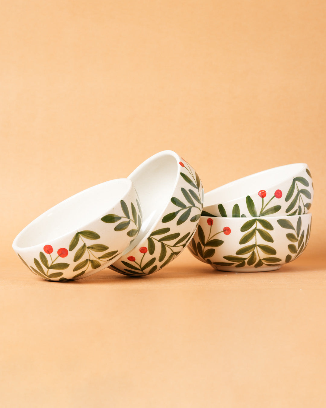 Three ceramic bowls with leaf and berry pattern on a beige background