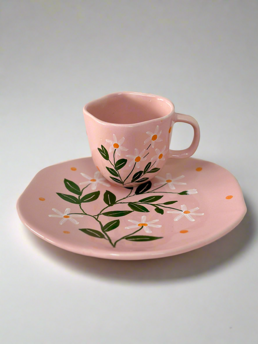 Pink ceramic cup and saucer with floral design on a white background