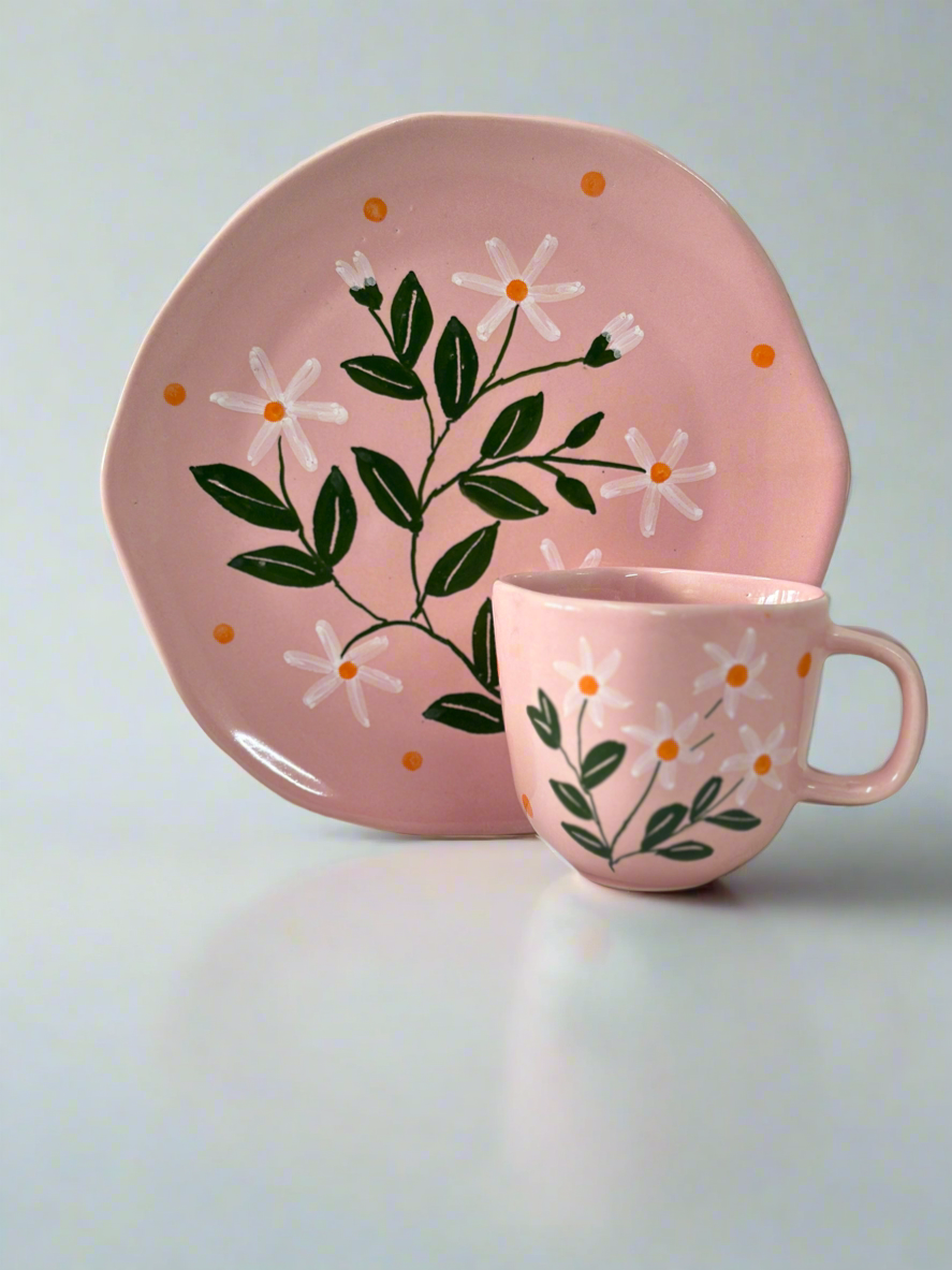 Pink ceramic mug and plate set with floral design on a light gray background