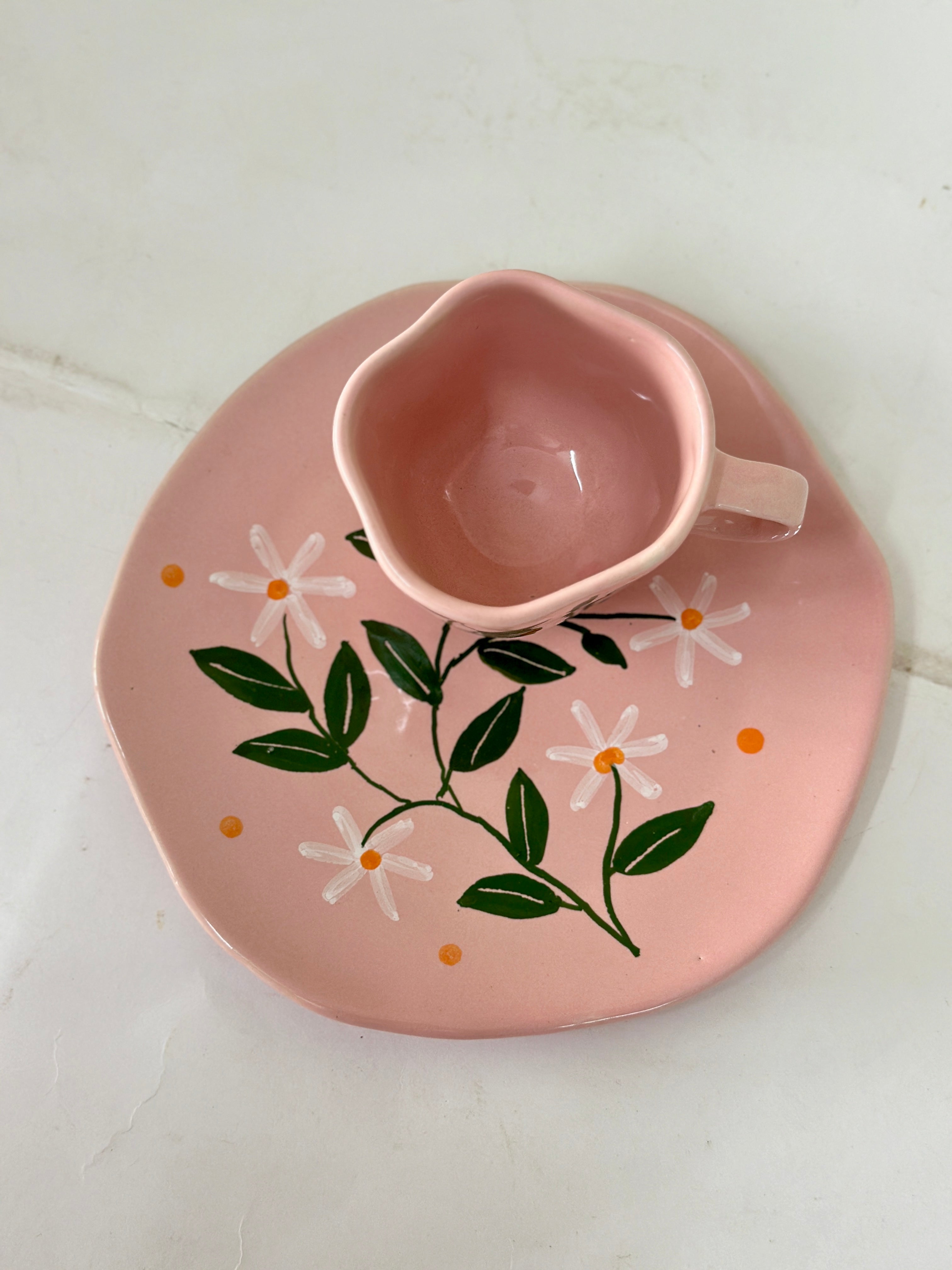 Pink ceramic cup and saucer with floral design on a white background