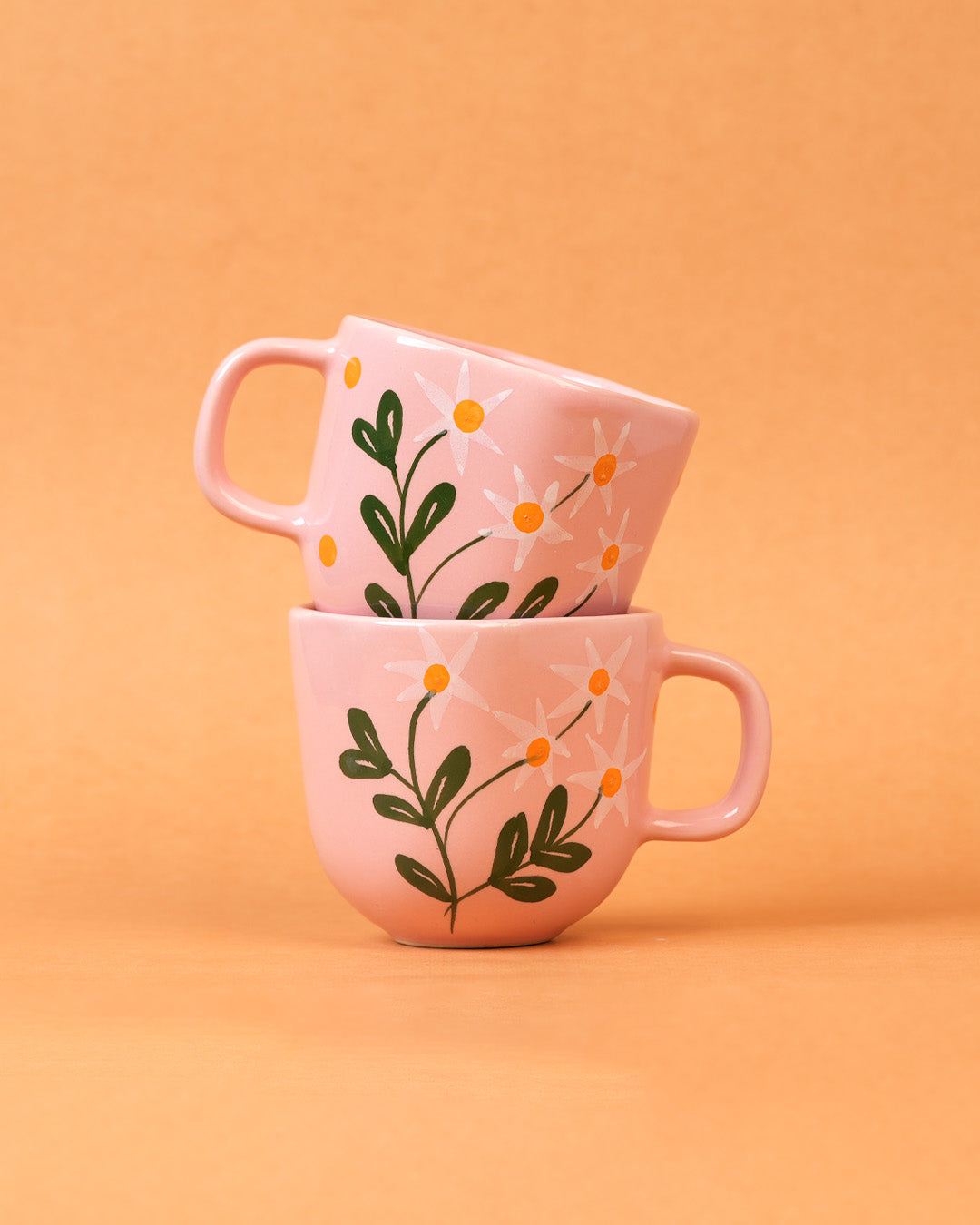 Two pink mugs with floral designs stacked on an orange background