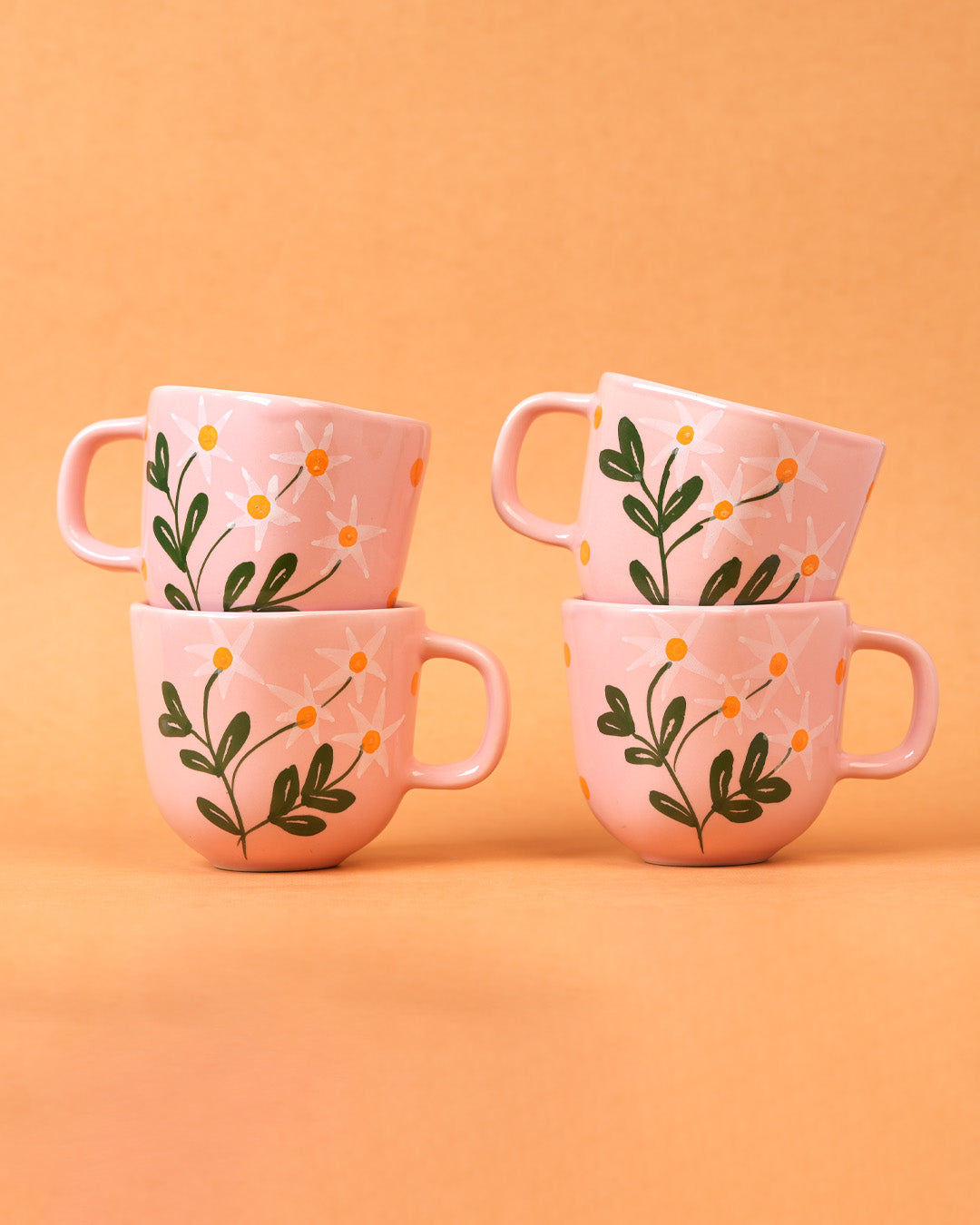 Set of four pink mugs with floral designs on a peach background