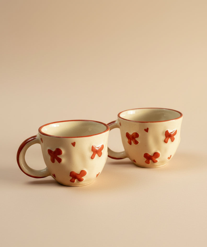 Two ceramic mugs with red butterfly designs on a beige background