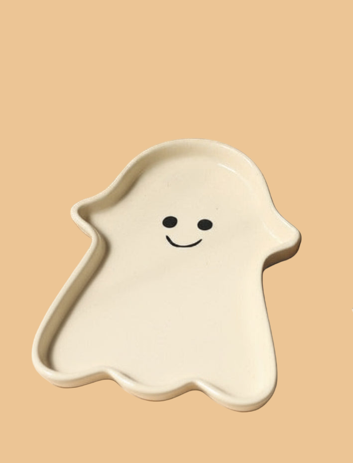Ceramic ghost-shaped plate with a smiley face on a beige background