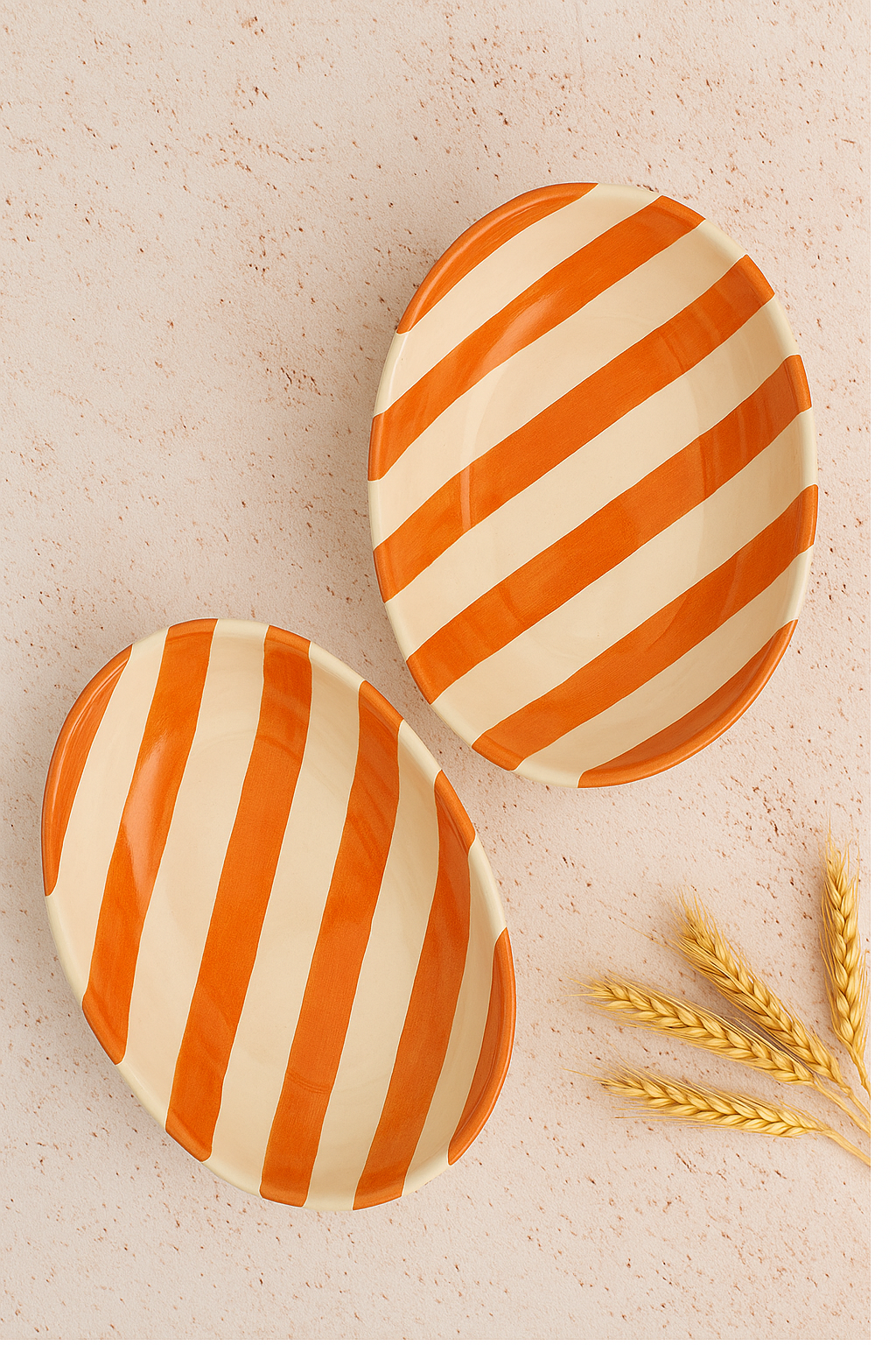 Two orange and white striped ceramic plates on a beige surface with wheat stalks.