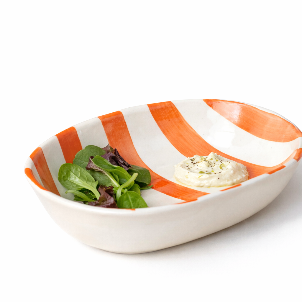 White bowl with orange stripes containing salad and a small dish of dressing on a white background
