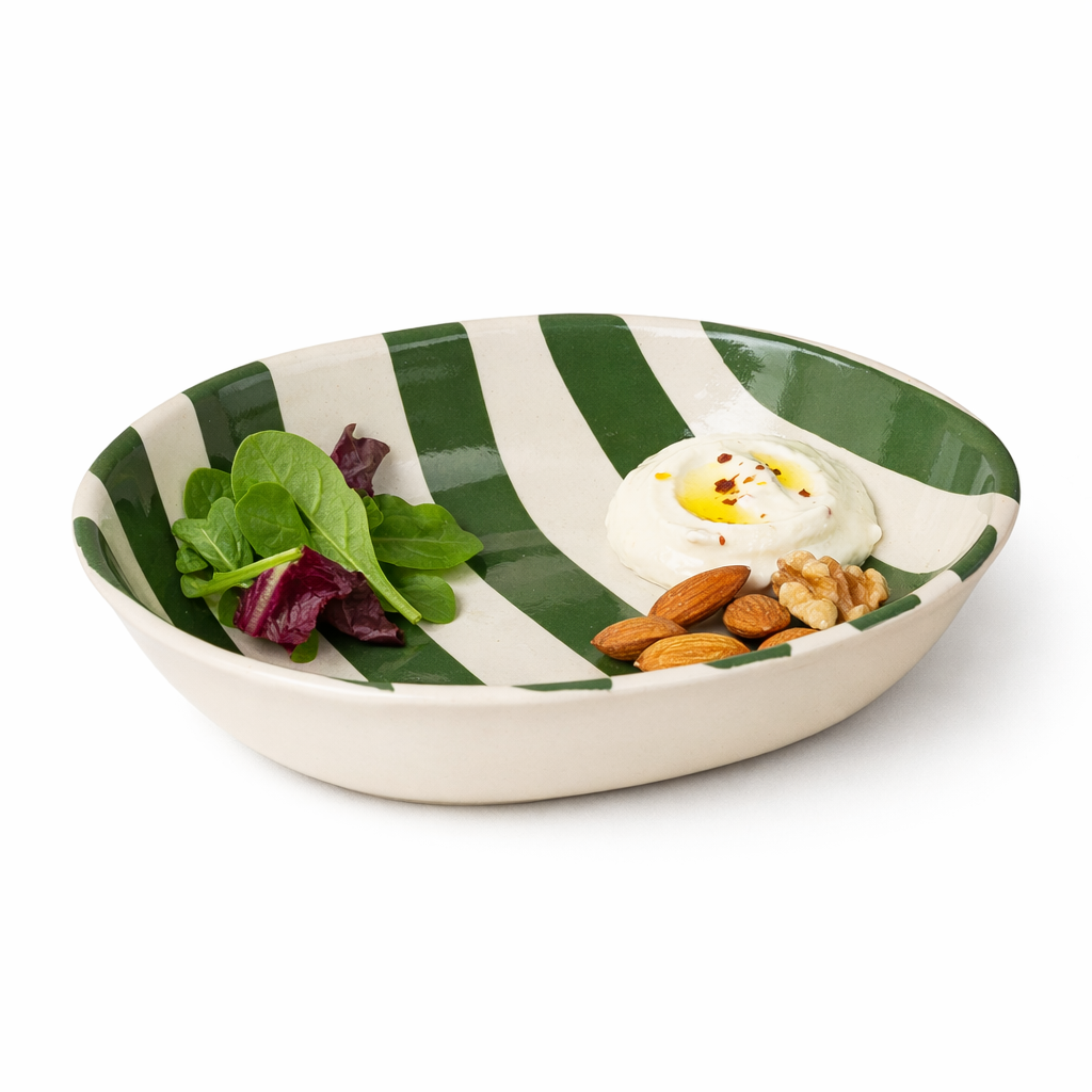 Green and white striped bowl with salad and nuts on a white background