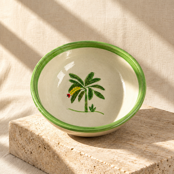 A round ceramic bowl with a light beige interior, a green rim, and a hand-painted green palm tree with a yellow and red caterpillar motif, shown from a top-down view on a white background.